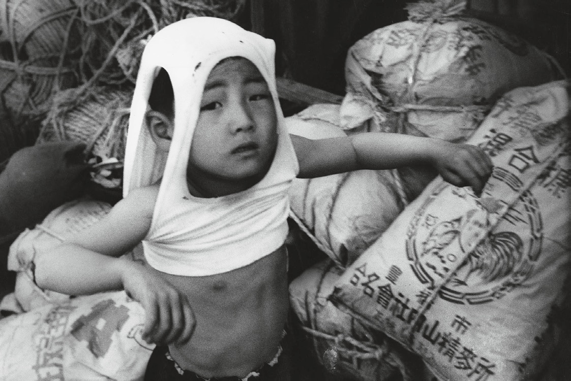 Nippori suburb. Sacks of grain, rope, a boy in an undershirt-helmet, Tokyo, 1961